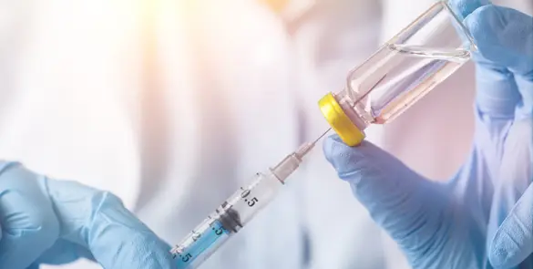 Close up of gloved hands extract a syringe of medication from a vial.