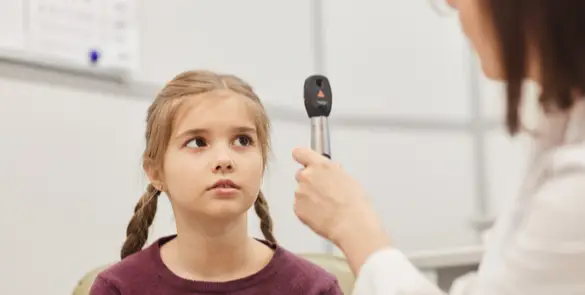 Paediatric eye check-up at Moorfields Dubai, with a clinician using a handheld light for red reflex assessment.
