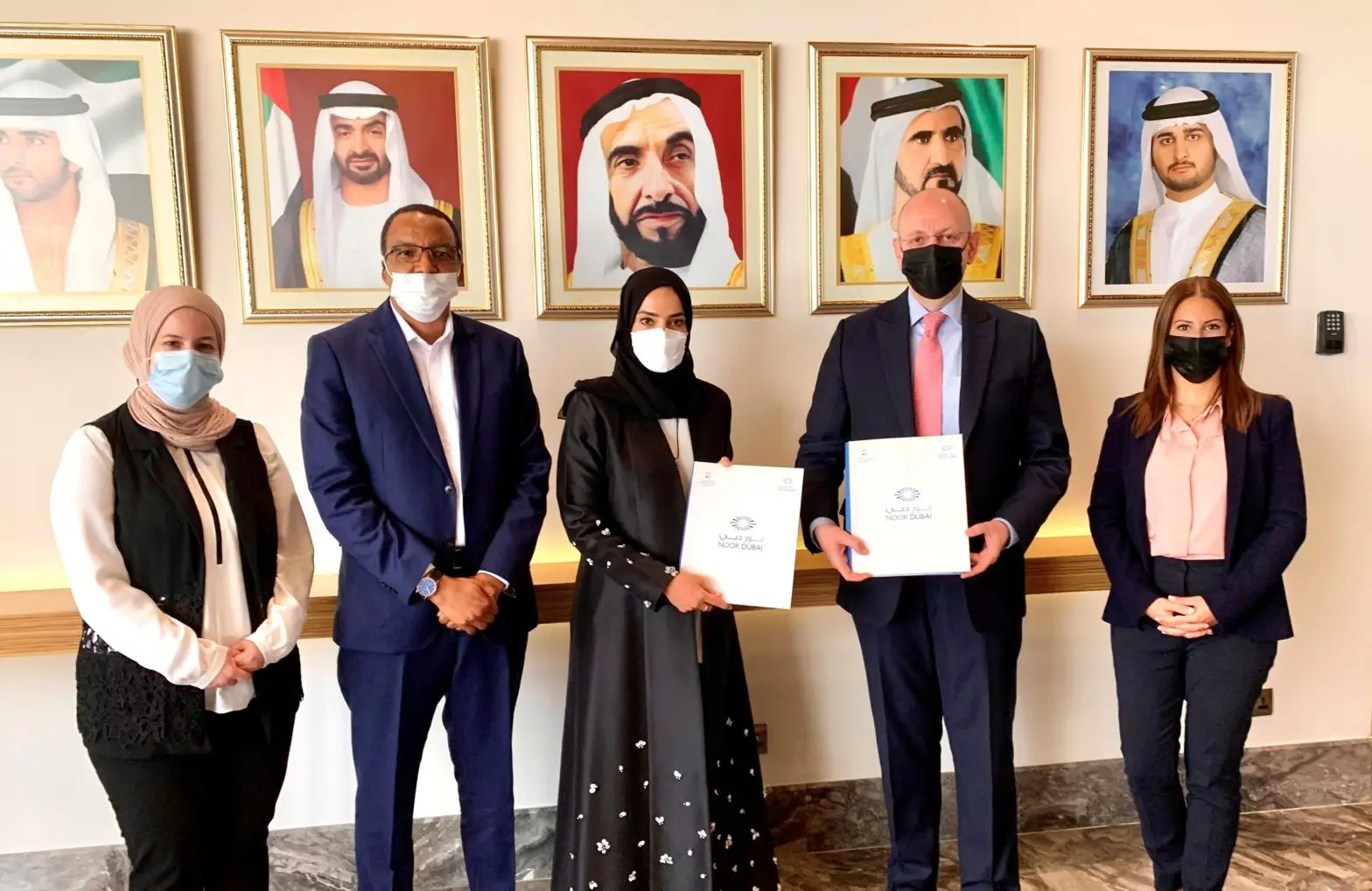 Group of six people in business attire wearing face masks standing and receiving certificates from Noor Dubai foundation for Moorfields Dubai during a celerbration event